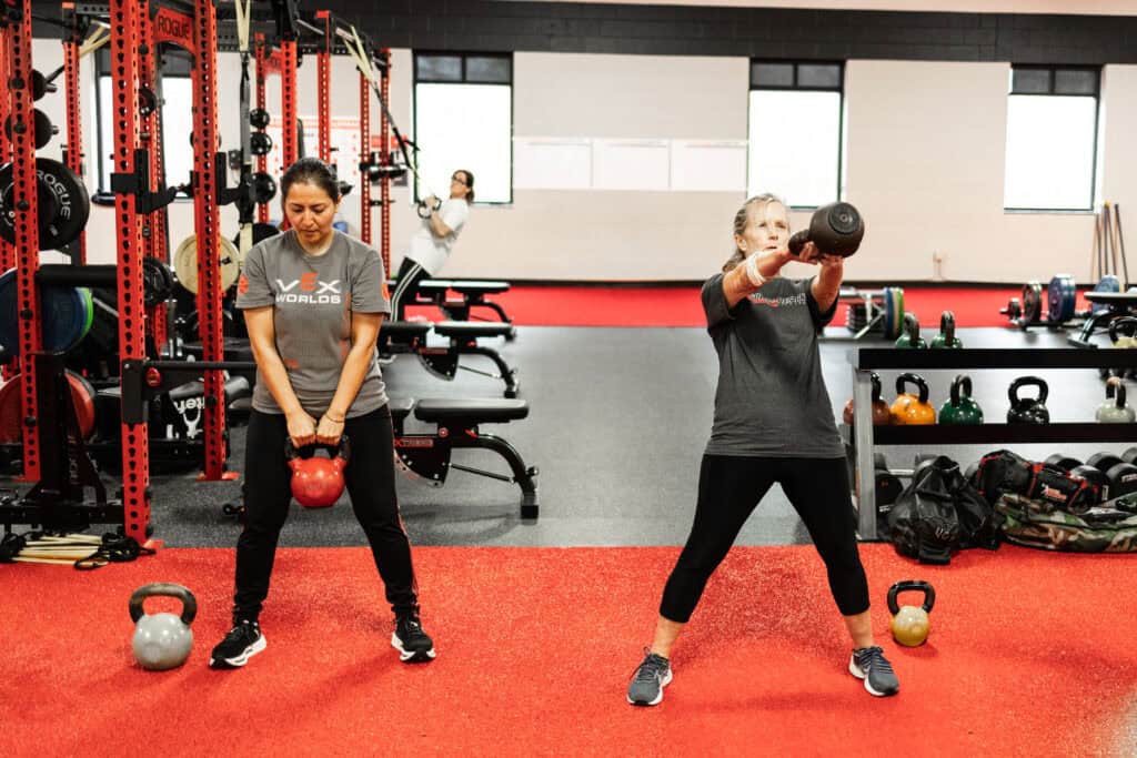 Two women performing kettlebell exercises at Results by Design Fitness, building strength and preserving muscle mass post weight loss.
